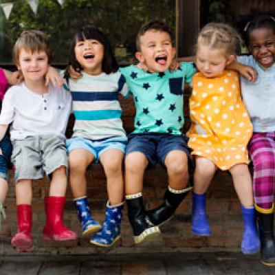 Six children, linked in arms smiling on a park bench 