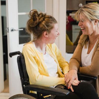 Disability worker kneeling beside a smiling lady in a wheelchair