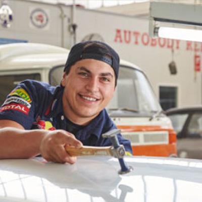 Auto repairer banging dents out of a car bonnet