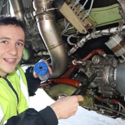 Apprentice stands at the engine of a large plane