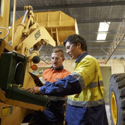 Two mechanics standing with a large bulldozer observing repairs