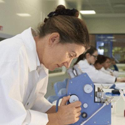 Lady wearing a white laboratory coat looking through a microscope