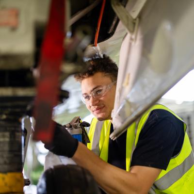 A student wearing safety glasses crouching down next to an aeroplane working on plane maintenance