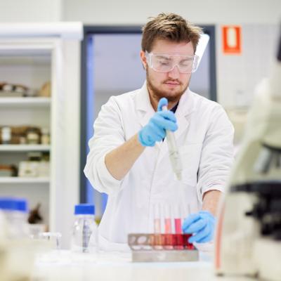 A student in lab technology wearing safety glasses and gloves using a pipette