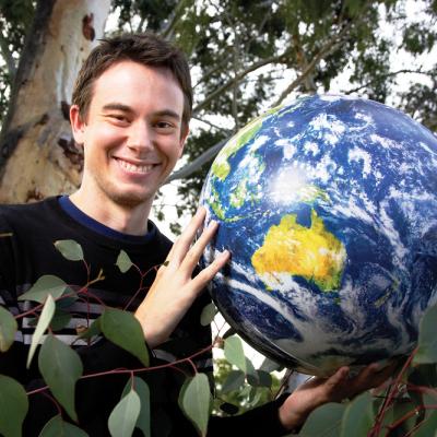 A horticulture student holds a world globe surrounded by green trees 