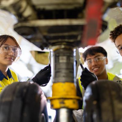 Three students looking at camera working underneath an airplane