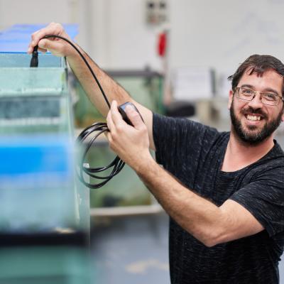 Aquaculture student smiling next to fishtank holding equipment