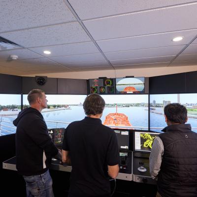 Three students looking out through a maritime simulator 