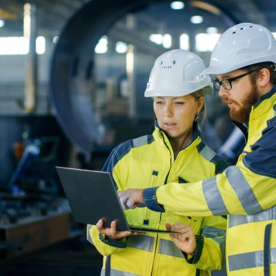 Two people in a hard hat and high vis looking at a laptop