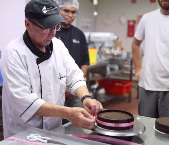 Image of a lecturer tying a pink ribbon around a chocolate cake