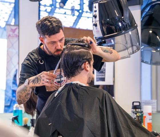Male barber cutting another male's hair who is seated in black cape