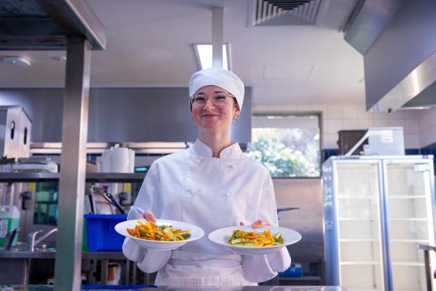 Cookery student Alexis holding two plates in the kitchen and smiling
