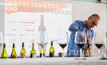 Wine industry lecturer pouring wine, infront of a projector in a classroom