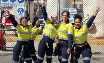 Five women's scholarship graduates posing for a photo infront of process plant