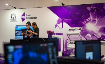Two lecturers looking at an iPad infront of South Metro TAFE signage at the Resources Technology Showcase